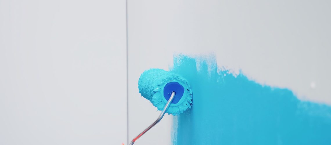 Roller brush on wall with blue paint. Apartment redecoration and home construction while renovating and improving. Repair and decorating.